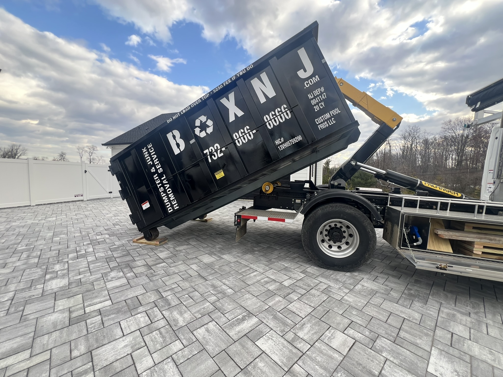 Tilted BoxNJ dumpster on machine.