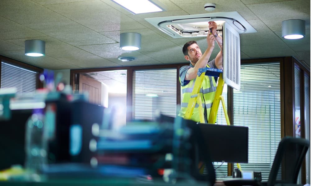 Maintenance worker adjusting air system within office building.